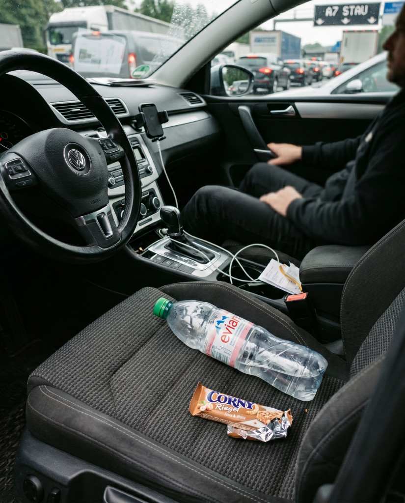 Wasserflasche und Energieriegel auf dem Beifahrersitz, im Hintergrund Stau auf der Autobahn | Alltagssicherheit